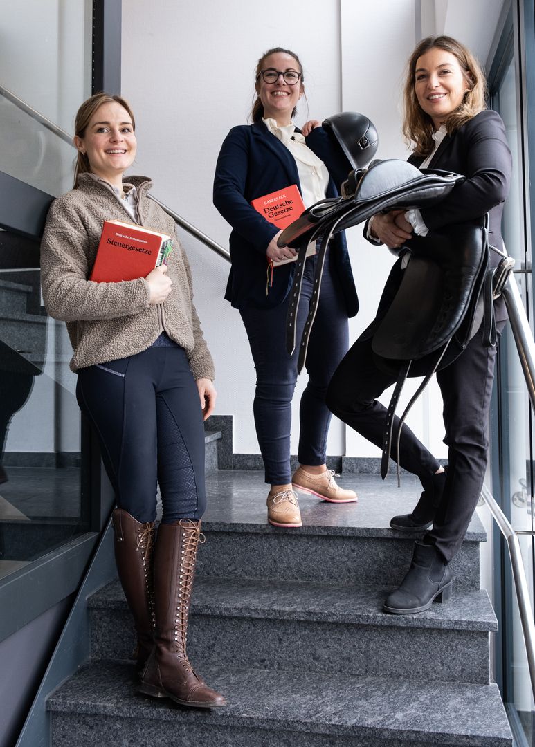Drei Personen stehen auf einer Treppe und lächeln in die Kamera